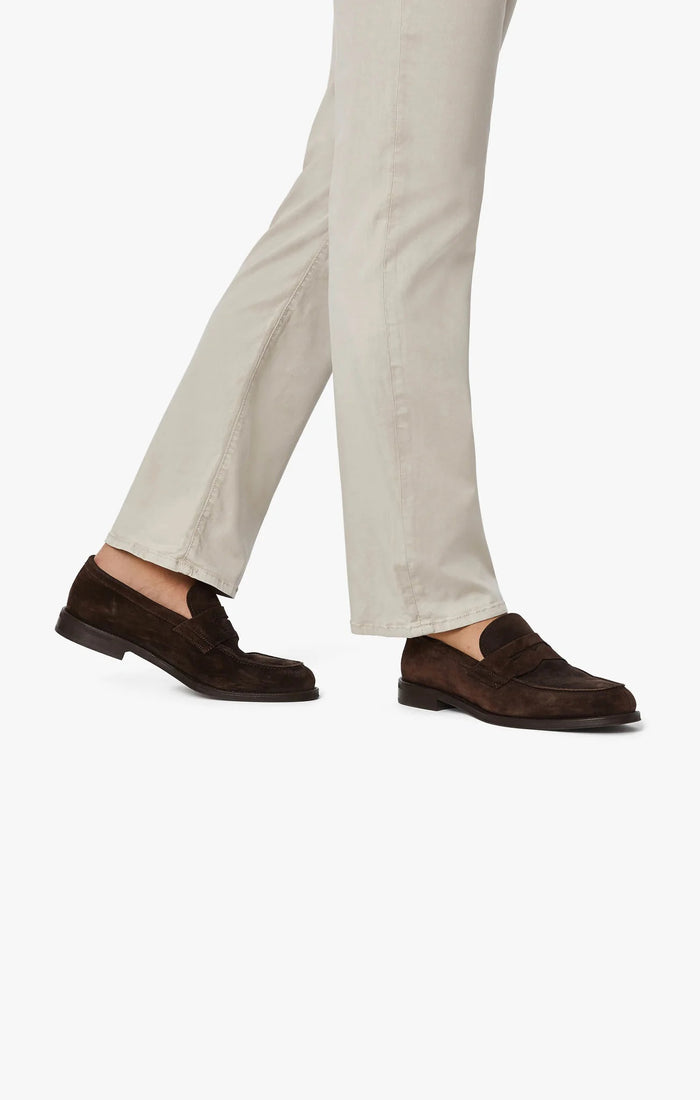 A man with light brown hair and a beard wears a tan blazer, brown sweater, white collared shirt, 34 HERITAGE - CHARISMA RELAXED STRAIGHT LEG PANT IN DAWN TWILL by 34 HERITAGE, and brown shoes against a plain white background.