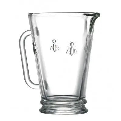 The BEE PITCHER by LA ROCHERE is a clear glass all-purpose pitcher with a round base, embossed bee designs, a graceful handle, and spout for easy pouring. The pitcher is empty.