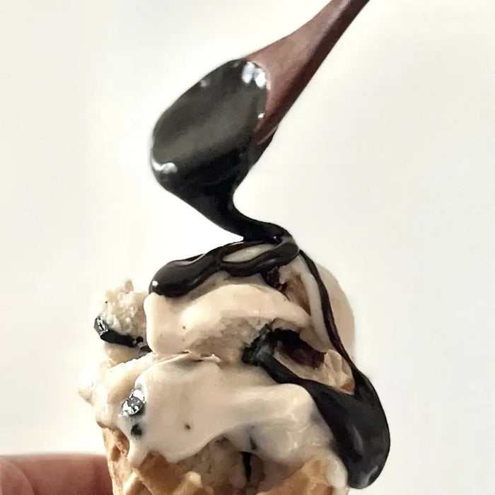 A jar of COOPS VEGAN HOT FUDGE features rich European chocolate fudge dripping down the side. The green label with pink lettering and a brown lid display the product name and description—ideal as an ice cream topping.