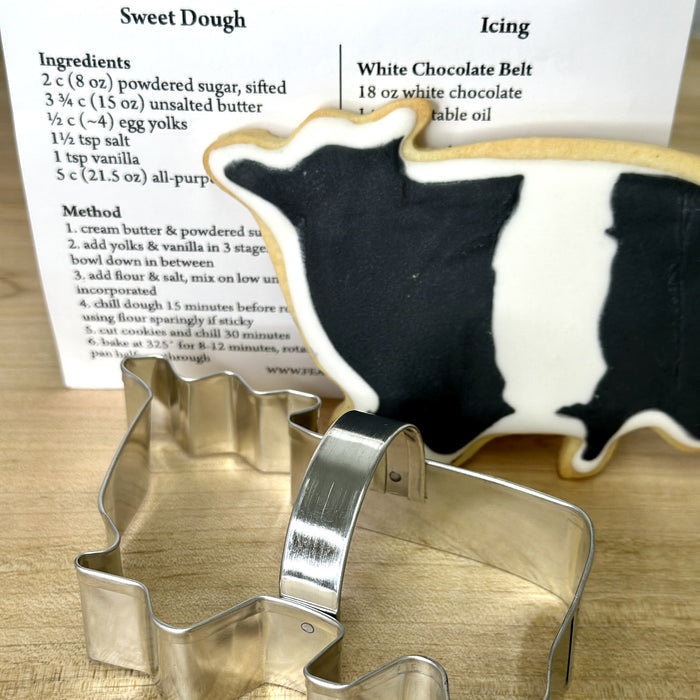 The FEARRINGTON SIGNATURE COLLECTION - BELTIE COOKIE CUTTER by AD RESOURCES is a metal Beltie-shaped cookie cutter in a clear bag, tied with a black-and-white striped ribbon, and includes a recipe card and "FEARINGTON" labeled card.