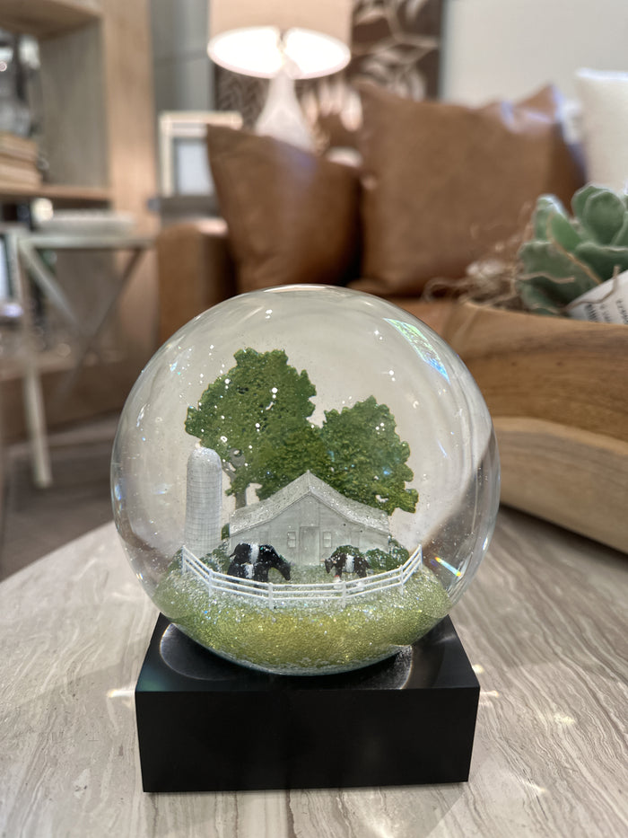 The FEARRINGTON SIGNATURE COLLECTION - FEARRINGTON BELTIE SNOWGLOBE by COOL SNOW GLOBES features a white barn, silo, cows, trees, and a white fence on a black base—a perfect Carolina gift for any collector.
