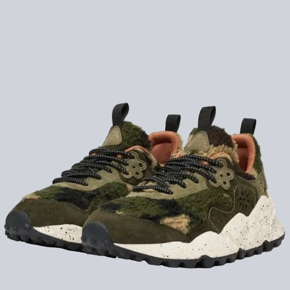 A pair of chunky sneakers with a green, brown, and tan camouflage pattern, black and white speckled soles, black laces, and pull tabs on the tongue and heel.