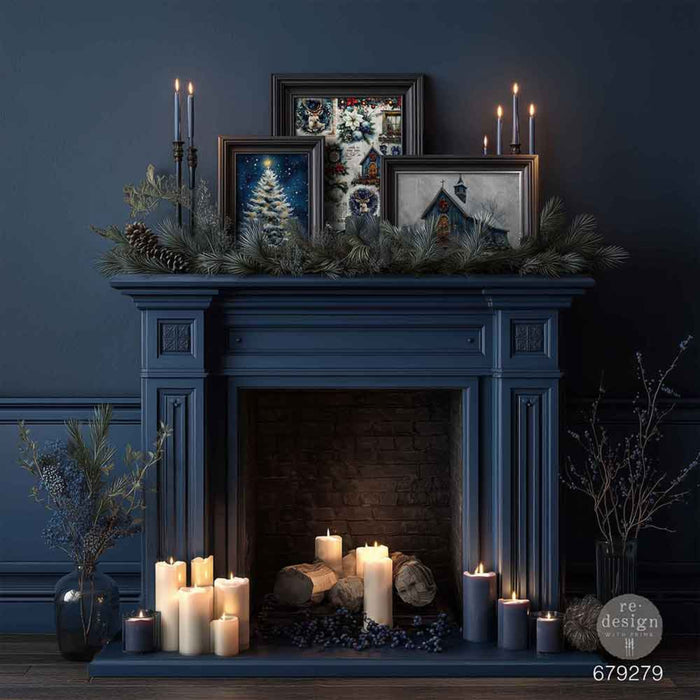 A dark blue fireplace mantel decorated with pine garland, framed winter-themed artwork, candles, and logs, set against a matching dark blue wall.