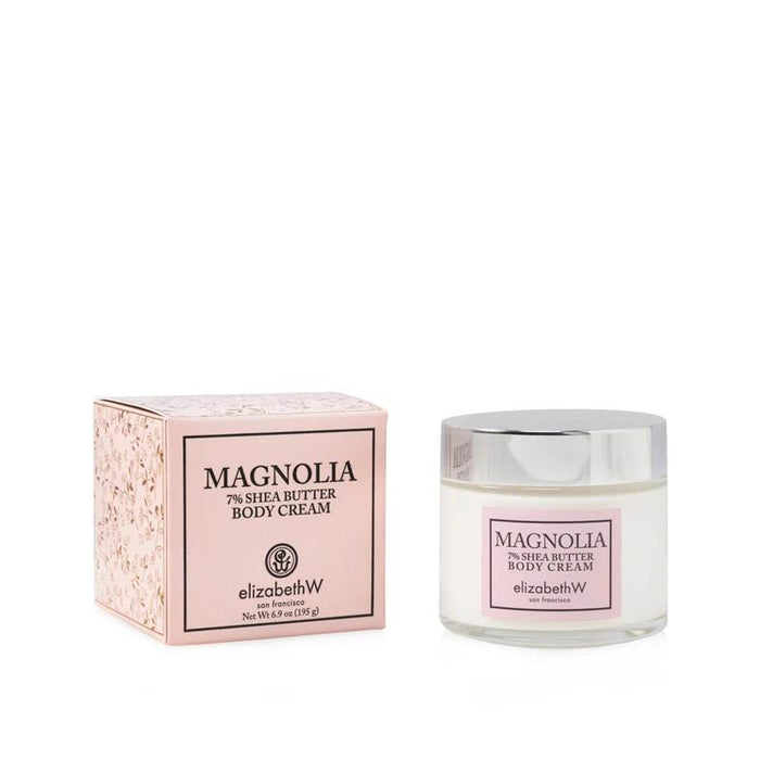 A jar of E WIGHTMAN & CO MAGNOLIA BODY CREAM with a silver lid sits beside its matching floral light pink box—an intensely hydrating botanical cream.