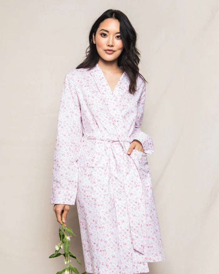 The PETITE PLUME - DORSET FLORAL ROBE by PETITE PLUME is a long-sleeved, knee-length cotton robe with a light pink and white floral pattern, shawl collar, and matching belt. Lightweight sleepwear shown on a white background.