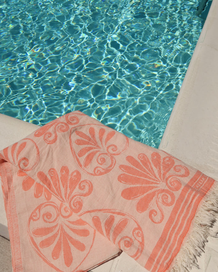Coral and cream Anthemion print cotton towel next to a pool, Greek pestemal towel scarf pareo