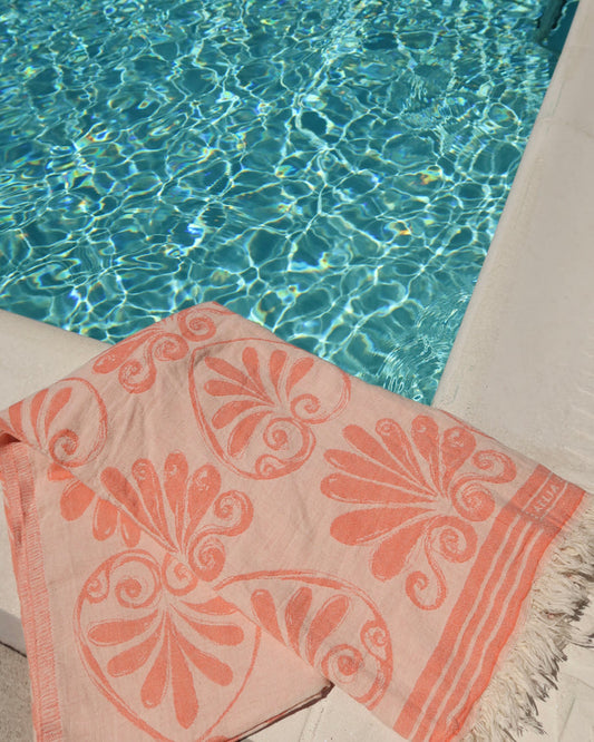 Coral and cream Anthemion print cotton towel next to a pool, Greek pestemal towel scarf pareo