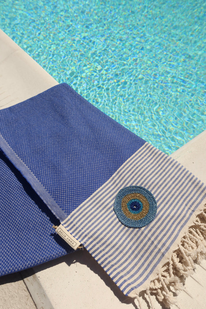 Blue and off-white striped cotton pestemal towel with an embroidered metallic evil eye and fringe trim made in Greece, Greek beach towel