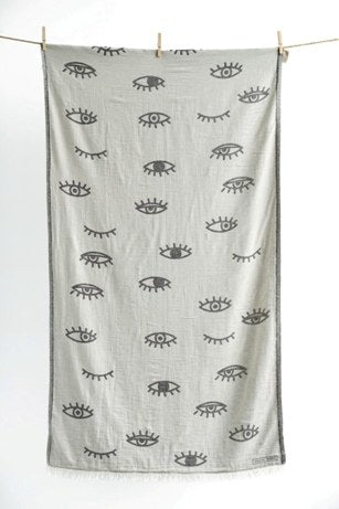 Gray white towel with black evil eye eye pattern hanging on a clothesline against a white background