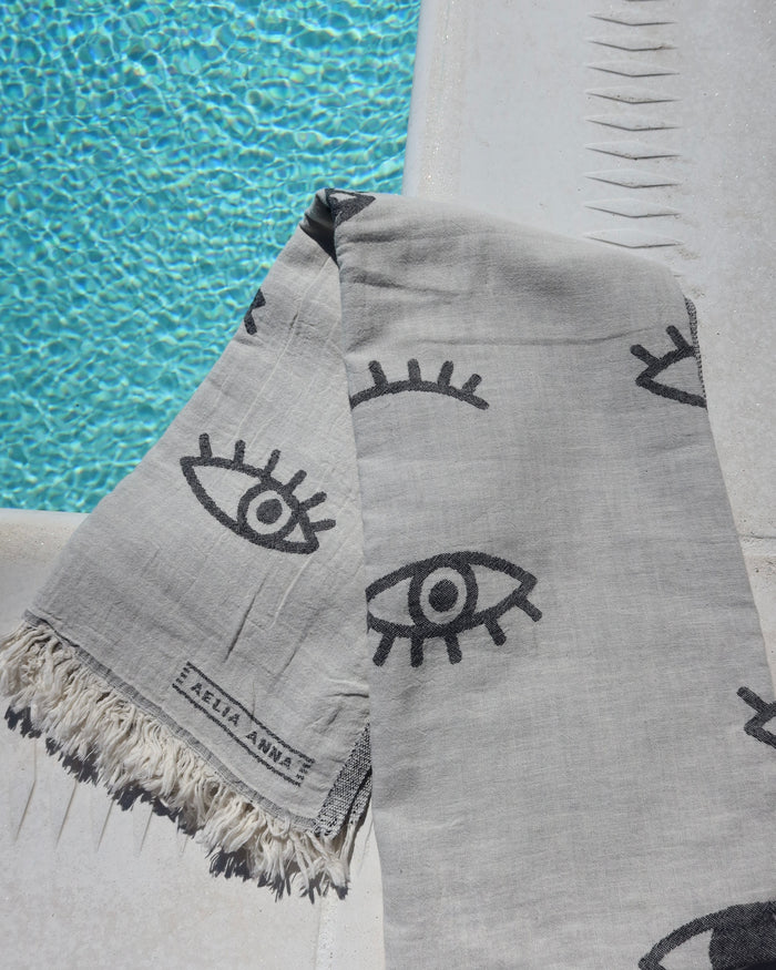 Gray towel with black evil eye pattern by a pool