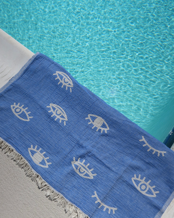 Blue cotton towel with white evil eye patterns on a poolside