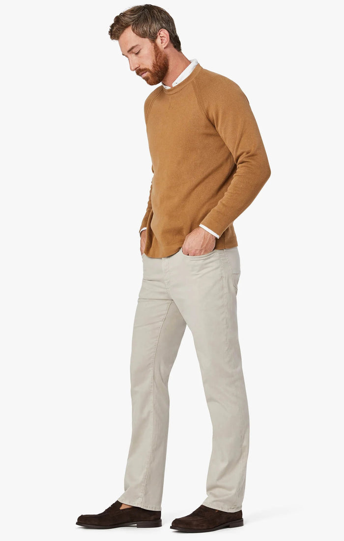 A man with light brown hair and a beard wears a tan blazer, brown sweater, white collared shirt, 34 HERITAGE - CHARISMA RELAXED STRAIGHT LEG PANT IN DAWN TWILL by 34 HERITAGE, and brown shoes against a plain white background.