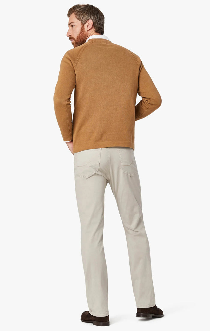 A man with light brown hair and a beard wears a tan blazer, brown sweater, white collared shirt, 34 HERITAGE - CHARISMA RELAXED STRAIGHT LEG PANT IN DAWN TWILL by 34 HERITAGE, and brown shoes against a plain white background.