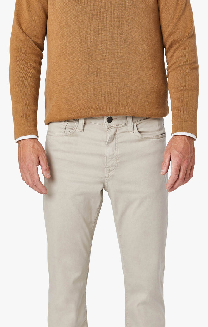 A man with light brown hair and a beard wears a tan blazer, brown sweater, white collared shirt, 34 HERITAGE - CHARISMA RELAXED STRAIGHT LEG PANT IN DAWN TWILL by 34 HERITAGE, and brown shoes against a plain white background.
