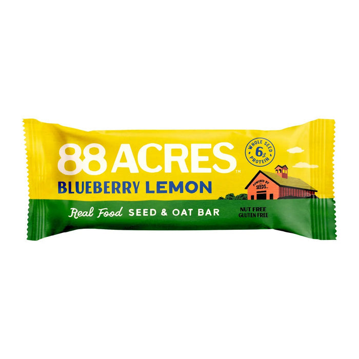 An 88 ACRES - BLUEBERRY LEMON SEED OAT BAR rests in its packaging on a white wooden surface, displaying images of blueberries and lemons. The gluten-free, vegan bar from 88 ACRES is nut-free, nutritious, and delicious.