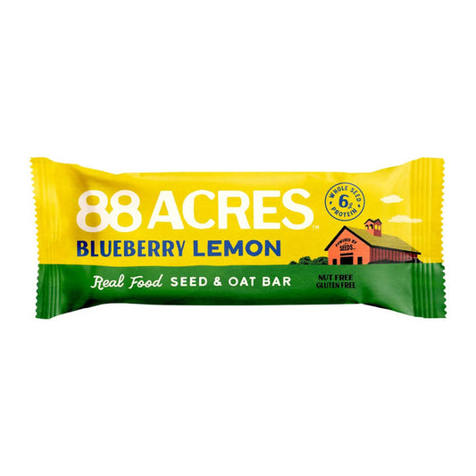 An 88 ACRES - BLUEBERRY LEMON SEED OAT BAR rests in its packaging on a white wooden surface, displaying images of blueberries and lemons. The gluten-free, vegan bar from 88 ACRES is nut-free, nutritious, and delicious.