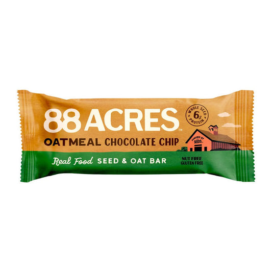 An 88 ACRES - OATMEAL CHOCOLATE CHIP SEED OAT BAR is shown on a light wooden surface, its brown and white wrapper featuring oats, chocolate chips, and Australian sea salt for a chewy cookie bar experience.