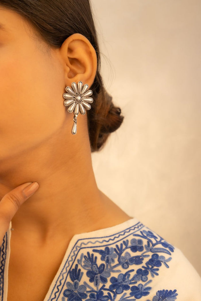 A person wearing a silver embossed flower petal drop earring.