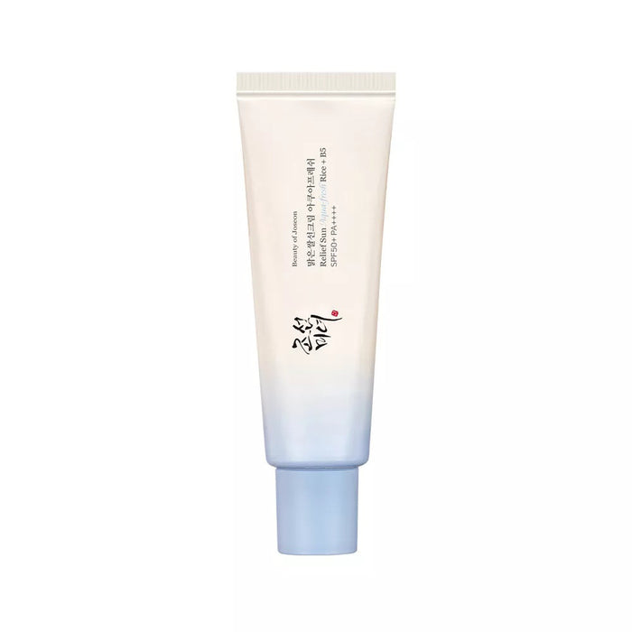 A person in a white tank top applies BEAUTY OF JOSEON - RELIEF SUN AQUA FRESH SPF50 by GLOWISS to their cheek. They hold the blue and white tube against a plain background, looking directly at the camera.