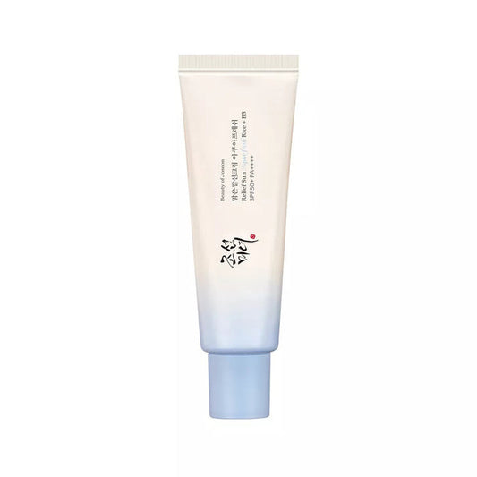 A person in a white tank top applies BEAUTY OF JOSEON - RELIEF SUN AQUA FRESH SPF50 by GLOWISS to their cheek. They hold the blue and white tube against a plain background, looking directly at the camera.