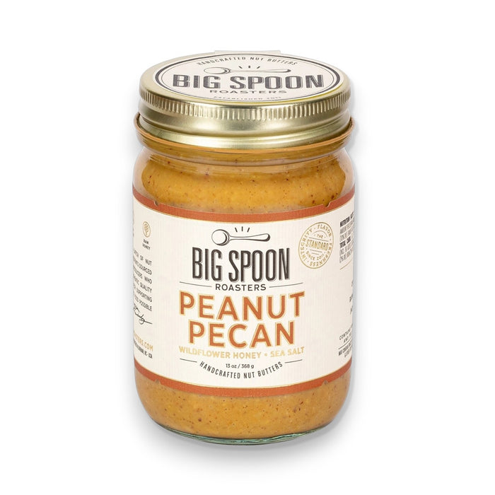A jar of BIG SPOON ROASTERS - PECAN PEANUT WILDFLOWER HONEY NUT BUTTER features wildflower honey, organic coconut oil, and sea salt. The gold lid and white label display the BIG SPOON ROASTERS brand and product details.