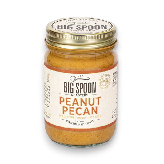 A jar of BIG SPOON ROASTERS - PECAN PEANUT WILDFLOWER HONEY NUT BUTTER features wildflower honey, organic coconut oil, and sea salt. The gold lid and white label display the BIG SPOON ROASTERS brand and product details.