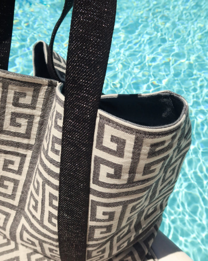 Tote bag with greek key meander pattern and black metallic silver strap by a pool
