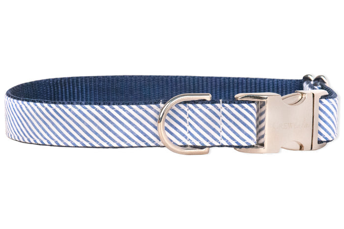A blue and white diagonal striped dog collar with a clean, nautical style. The exterior seersucker fabric features narrow  stripes, while the interior is lined with durable navy nylon webbing. The collar includes a silver metal D-ring for leash attachment and a sturdy side-release buckle engraved with the brand name “Crew LaLa.” The stitching is precise, with reinforced sections near the hardware for added strength and durability.