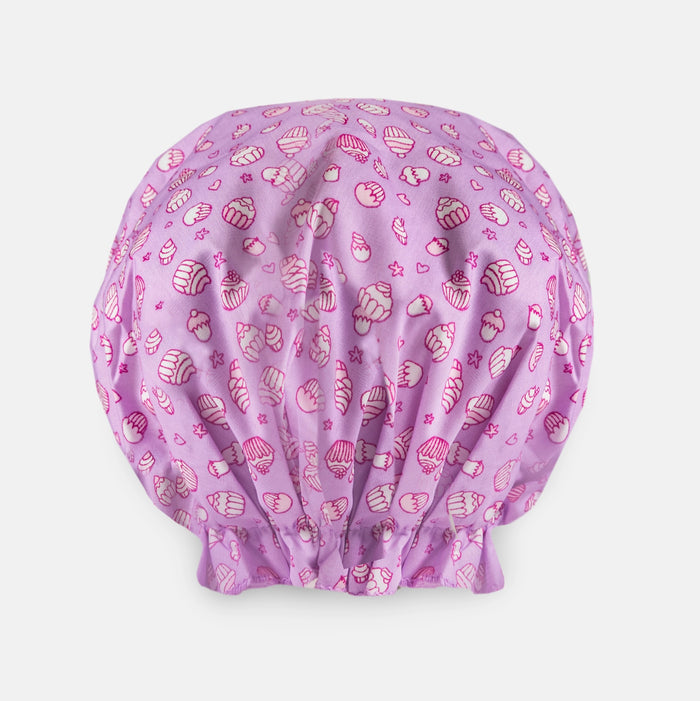 The BOUFFANT SHOWER CAP - CUPCAKES by BATH ACCESSORIES COMPANY features a pink waterproof design with a playful cupcake pattern on a light background.