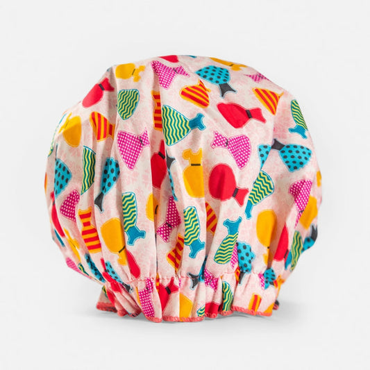 The BATH ACCESSORIES COMPANY BOUFFANT SHOWER CAP - DRESSES is a waterproof cap with a playful multicolored pattern on a light background and an elasticized bottom for a snug fit.