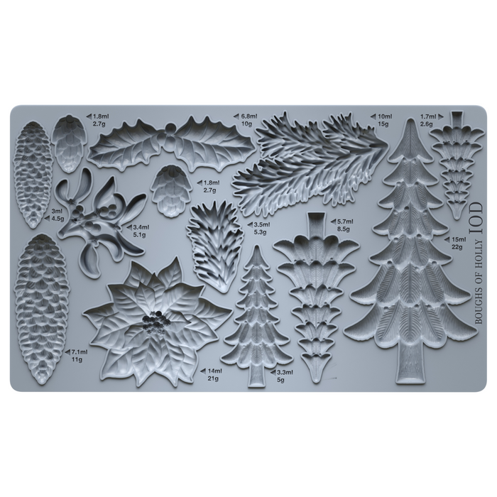 A gray silicone baking or craft mold tray with multiple embossed holiday botanical and tree shapes, including pinecones, holly leaves, mistletoe, and Christmas trees, each labeled with volume and weight measurements.