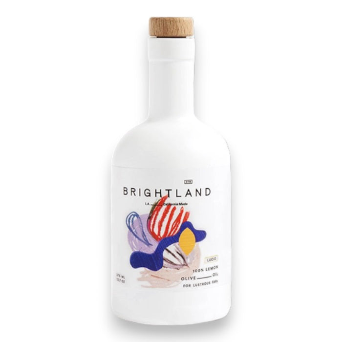 A white bottle of BRIGHTLAND ‘LUCID’ Lemon Infused Olive Oil with a wooden cap and a colorful abstract label. Crafted on California’s Central Coast for vibrant hair, this cold-pressed oil features zesty lemon flavor.