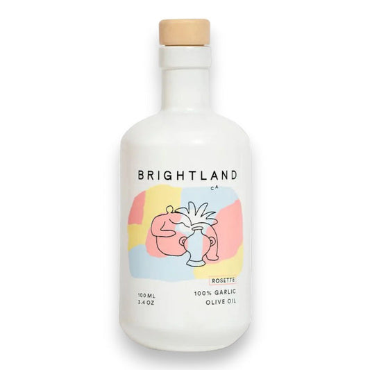 A white bottle of BRIGHTLAND 'ROSETTE' Garlic Infused Olive Oil with a wooden cap and a minimalist label featuring abstract line art, made from California olives.