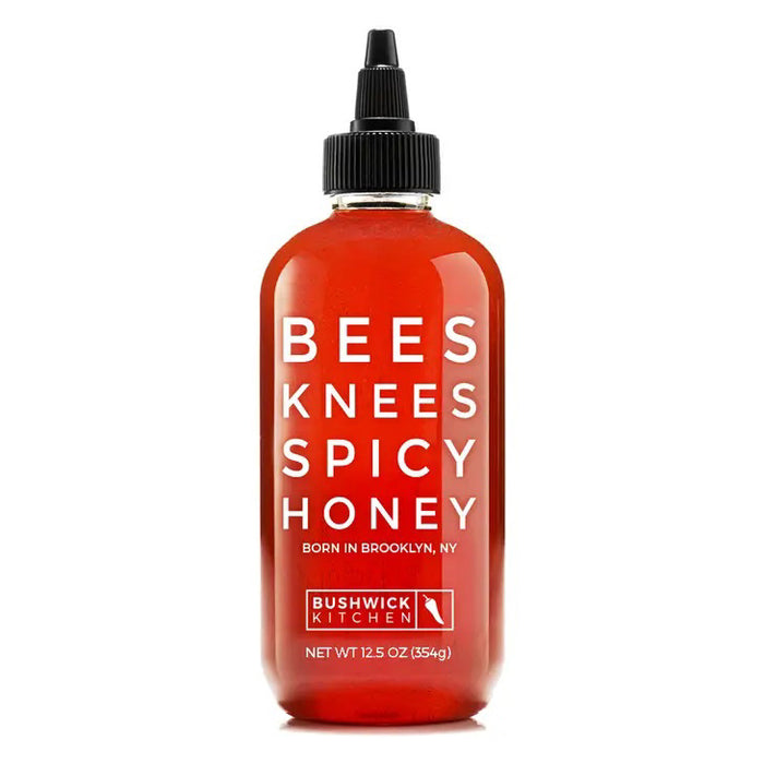 A 12.5 oz (354g) bottle of BUSHWICK KITCHEN - 'BEES KNEES' SPICY HONEY by BUSHWICK KITCHEN features an amber-colored honey visible through the clear container and a black twist cap. The label proudly states, "Born in Brooklyn, NY." This product is ideal for any honey gift set or for those who enjoy wildflower honeys with a spicy kick.