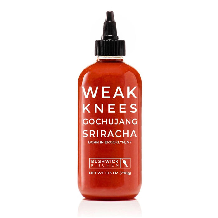 A clear bottle of BUSHWICK KITCHEN - 'WEAK KNEES' GOCHUJANG SRIRACHA hot sauce with a black squeeze cap, vibrant red chile paste, and label showing the name, "Born in Brooklyn, NY." Net wt. 10.5 oz (298g).