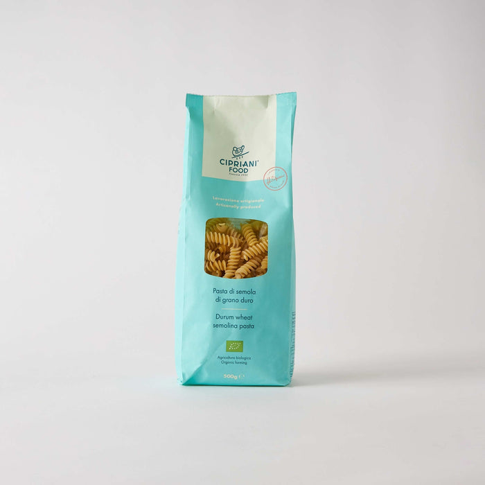 A turquoise bag of ATALANTA CORPORATION CIPRIANI - ORGANIC DURUM WHEAT FUSILLI stands upright on a white background, with the high protein pasta made using a traditional copper die visible through a clear window on the front.