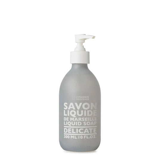 A 10oz glass pump bottle of COMPAGNIE DE PROVENCE - SAVON LIQUID DE MARSEILLE DELICATE by CIE LUXE BRANDS, featuring white text and a white dispenser, crafted with botanical oils for a gentle cleanse.