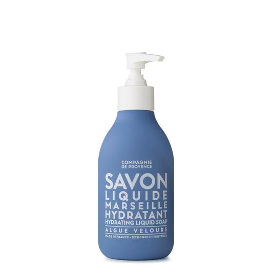 A blue pump bottle labeled "COMPAGNIE DE PROVENCE - SAVON LIQUIDE DE MARSEILLE VELVET SEAWEED 10OZ" by CIE LUXE BRANDS, featuring white text, stands upright against a white background—this is a luxurious liquid Marseille soap.