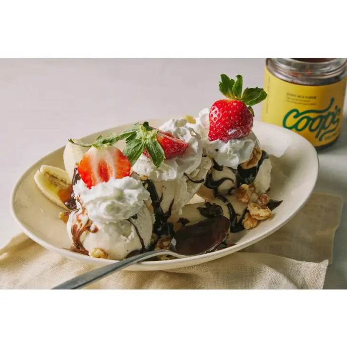 A jar of COOP'S - ORIGINAL HOT FUDGE is displayed with a dark brown lid and yellow label. The lid features a drip effect, resembling fudge oozing down the sides. The label boasts "Deep Rich Flavor, high-quality European chocolate with pure cream." This artisanal treat has a net weight of 10 ounces (283.5g).