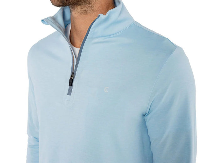 A man wears the CRIQUET Feather Performance Knit Quarter Zip Pullover in Heather Blue, featuring brrr° technology and a small embroidered logo on the chest, over a white T-shirt. His face is partially out of frame.