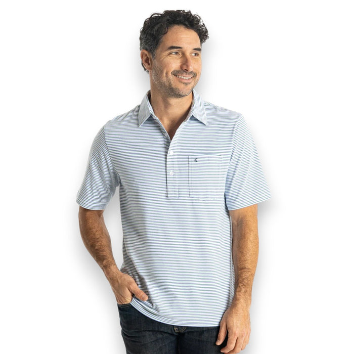 A person in sunglasses wears the CRIQUET Top-Shelf Players Shirt in Stewart Stripe White, standing by a countertop with a green can against blue-gray tiled walls.