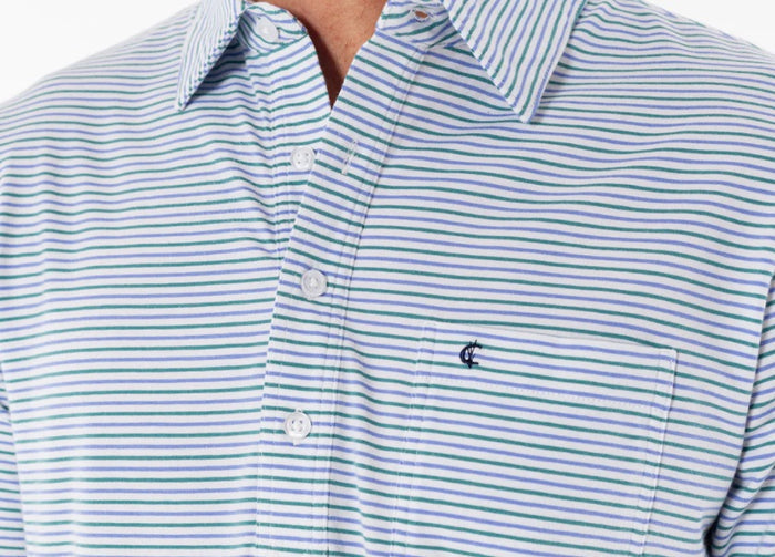A person in sunglasses wears the CRIQUET Top-Shelf Players Shirt in Stewart Stripe White, standing by a countertop with a green can against blue-gray tiled walls.