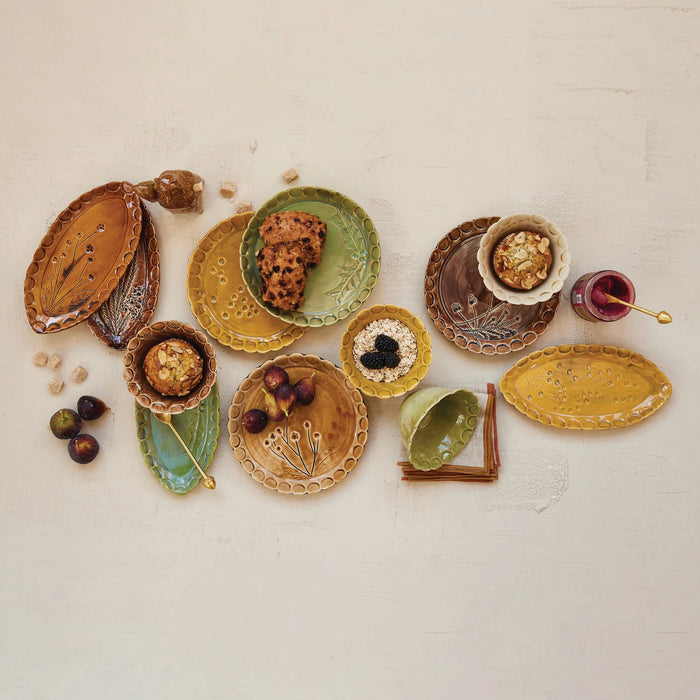 Four CREATIVE COOP DEBOSSED STONEWARE SCALLOPED PLATES with botanical designs and scalloped edges in brown, orange, green, and yellow, arranged in a square on a white background.