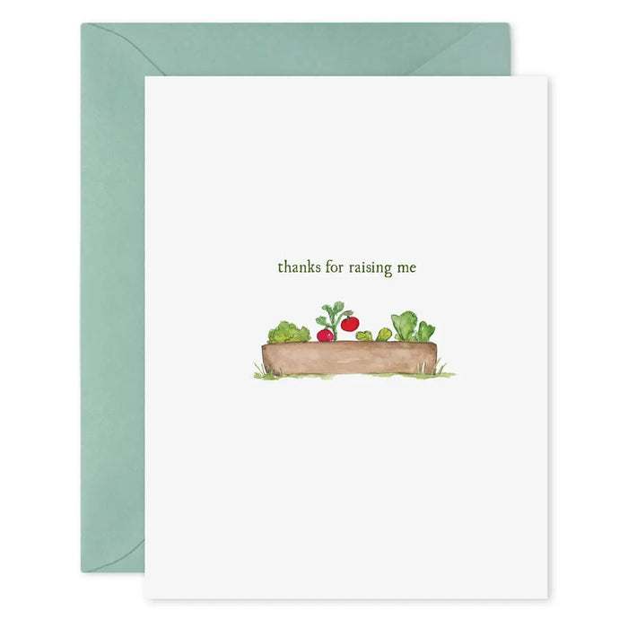 The E. FRANCES - THANKS FOR RAISING ME CARD by E. FRANCES PAPER is a hand-painted watercolor greeting card featuring a wooden garden bed with vegetables and the phrase "thanks for raising me," paired with a light blue envelope.