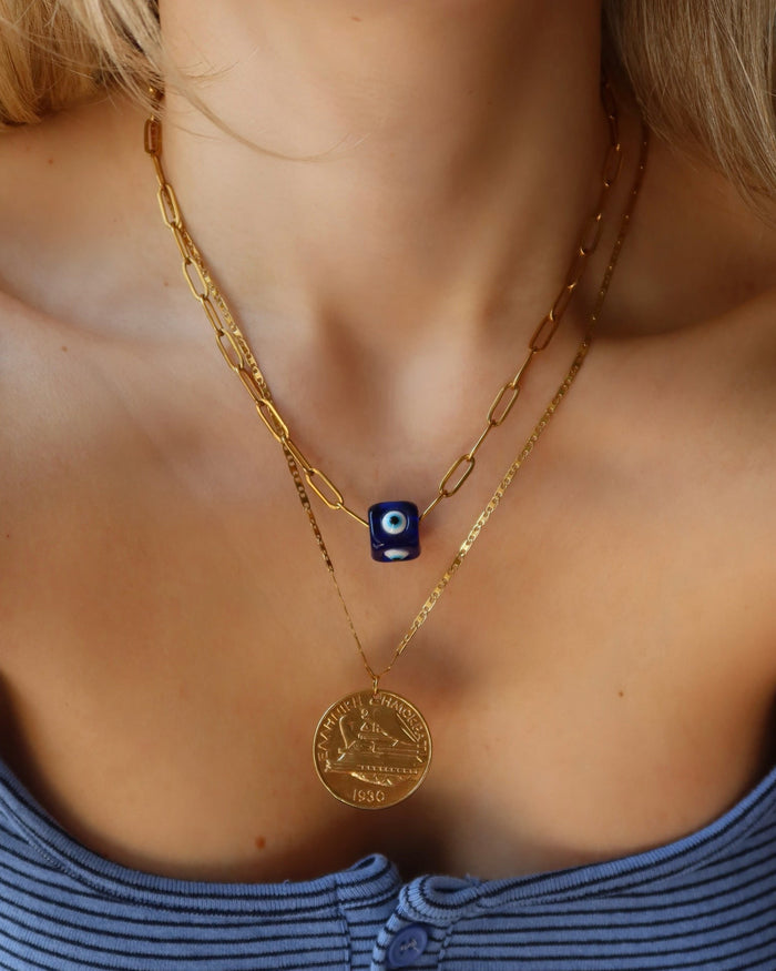Woman wearing a gold Drachma coin necklace and a blue evil eye bead necklace on a gold paperclip chain made in Greece; Greek jewelry