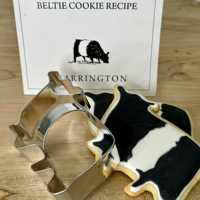 The FEARRINGTON SIGNATURE COLLECTION - BELTIE COOKIE CUTTER by AD RESOURCES is a metal Beltie-shaped cookie cutter in a clear bag, tied with a black-and-white striped ribbon, and includes a recipe card and "FEARINGTON" labeled card.