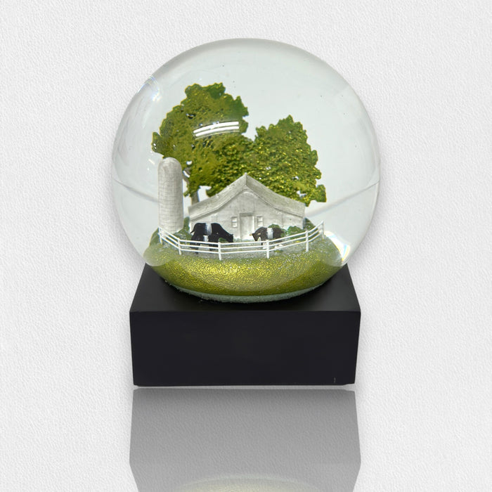The FEARRINGTON SIGNATURE COLLECTION - FEARRINGTON BELTIE SNOWGLOBE by COOL SNOW GLOBES features a white barn, silo, cows, trees, and a white fence on a black base—a perfect Carolina gift for any collector.