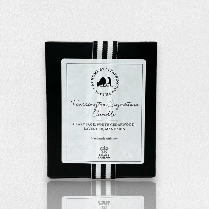 A sleek black box holds the FEARRINGTON SIGNATURE CANDLE by FEARRINGTON VILLAGE - HOME DECOR, with a white label and striped ribbon, featuring clary sage, white cedarwood, lavender, and mandarin scents.