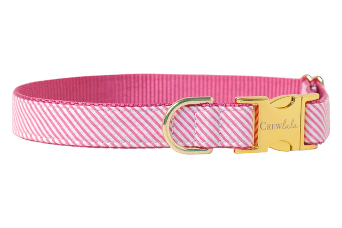A chic seersucker dog collar featuring diagonal fuchsia and white stripes, backed with durable pink nylon webbing. It’s finished with shiny gold-tone hardware, including a D-ring for leash attachment and a metallic side-release buckle engraved with “Crewlala”—perfect for pups who like their fashion as polished as their personality.