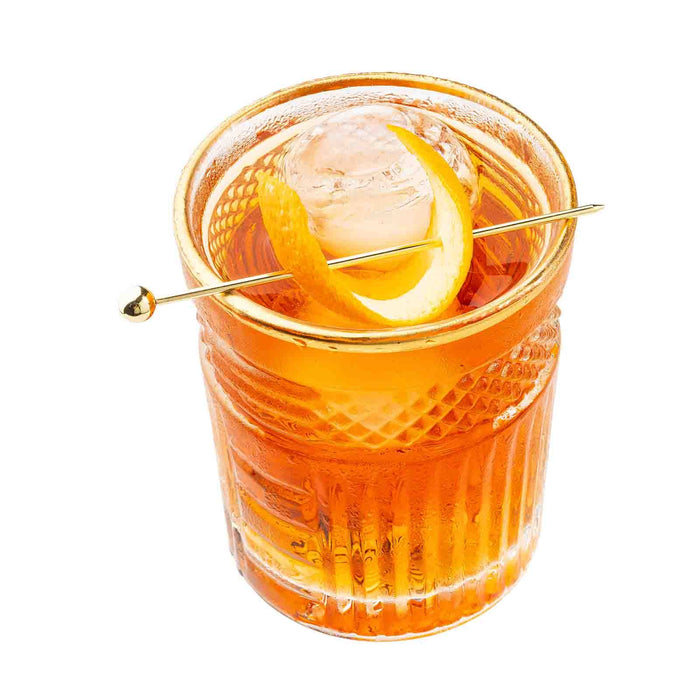 The Gold Cocktail Pick piecing an orange peel on top of a cocktail.